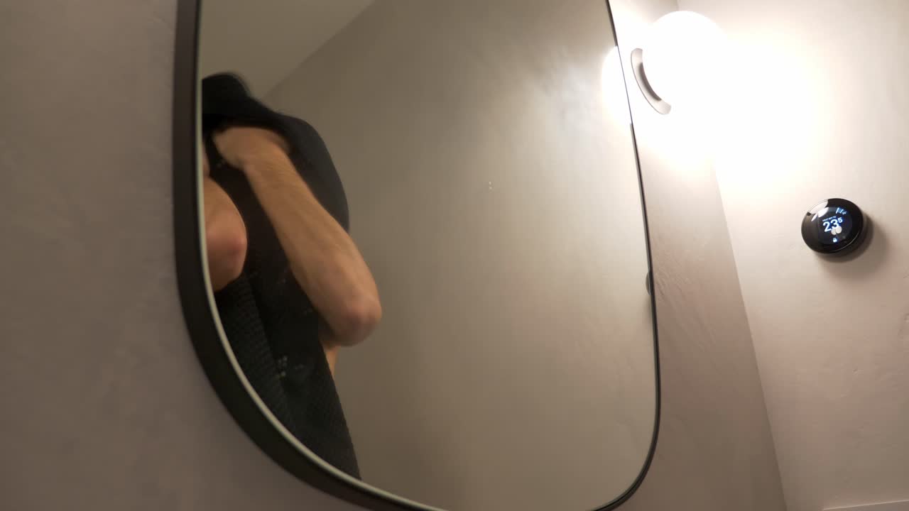 옷을 벗은 남자가 거울을 보고 샤워 후 수건으로 머리카락을  ⁇ 고 있다