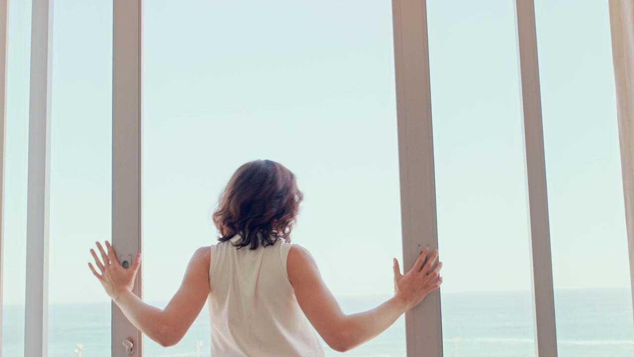 Woman Opening Large Window Overlooking the Ocean