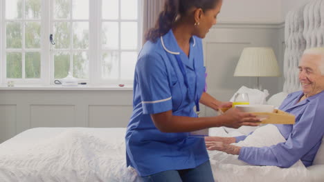 female care worker in uniform bringing senior man at home breakfast in bed on tray