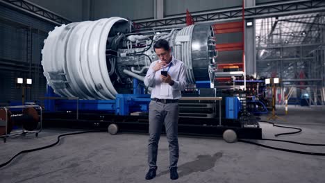full body of asian male professional worker with his smartphone with airplane engine maintenance conducted, analytics checking the turbine, he is nodding his head with dissapionted