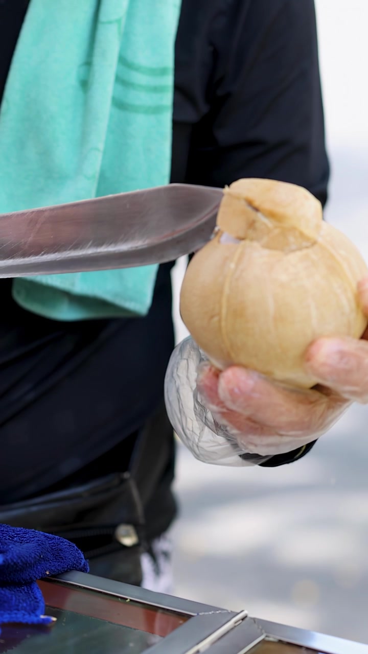 Penjual bersarung tangan dengan terampil membelah kelapa menggunakan parang di pasar terbuka, cahaya alami, tampilan dekat.