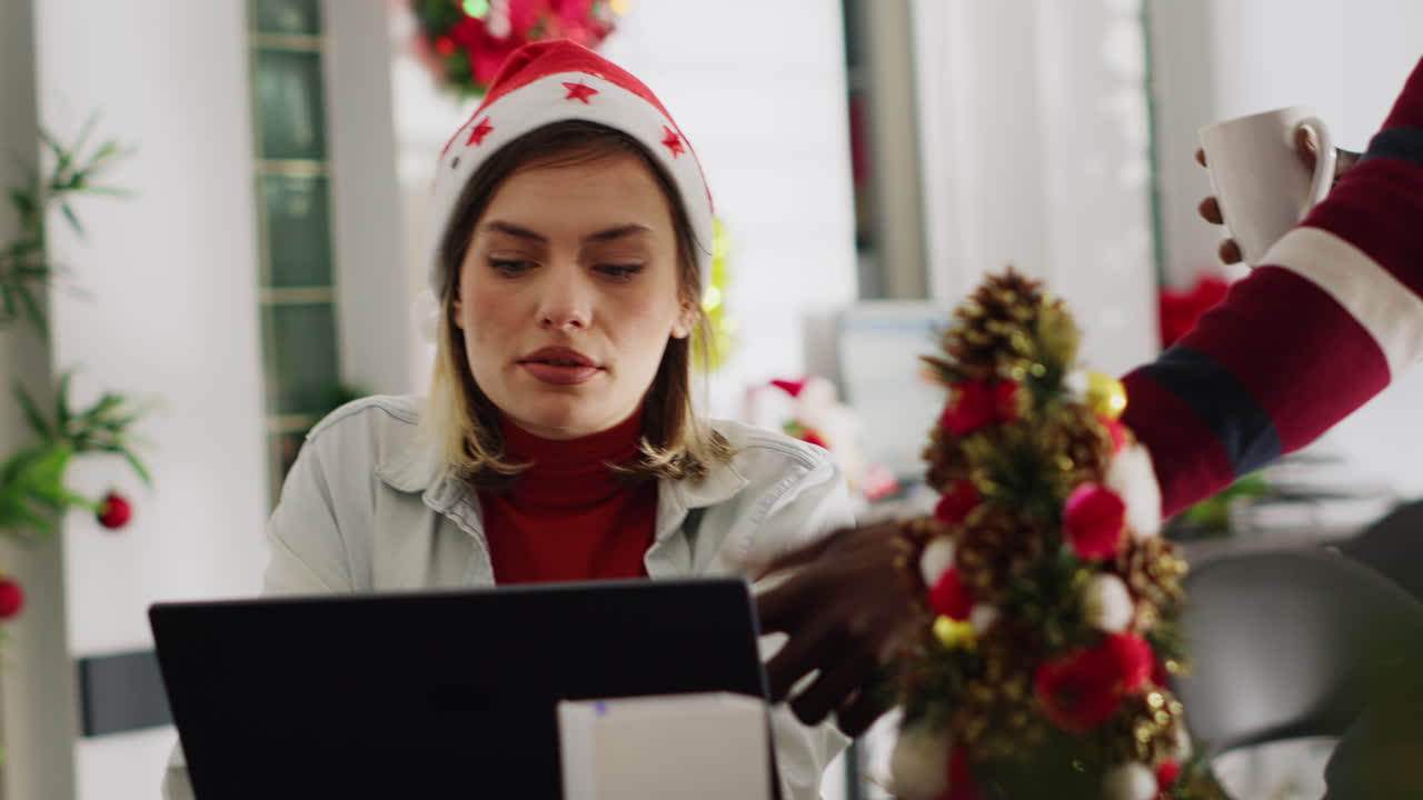 Woman in Santa hat working on laptop in festive office