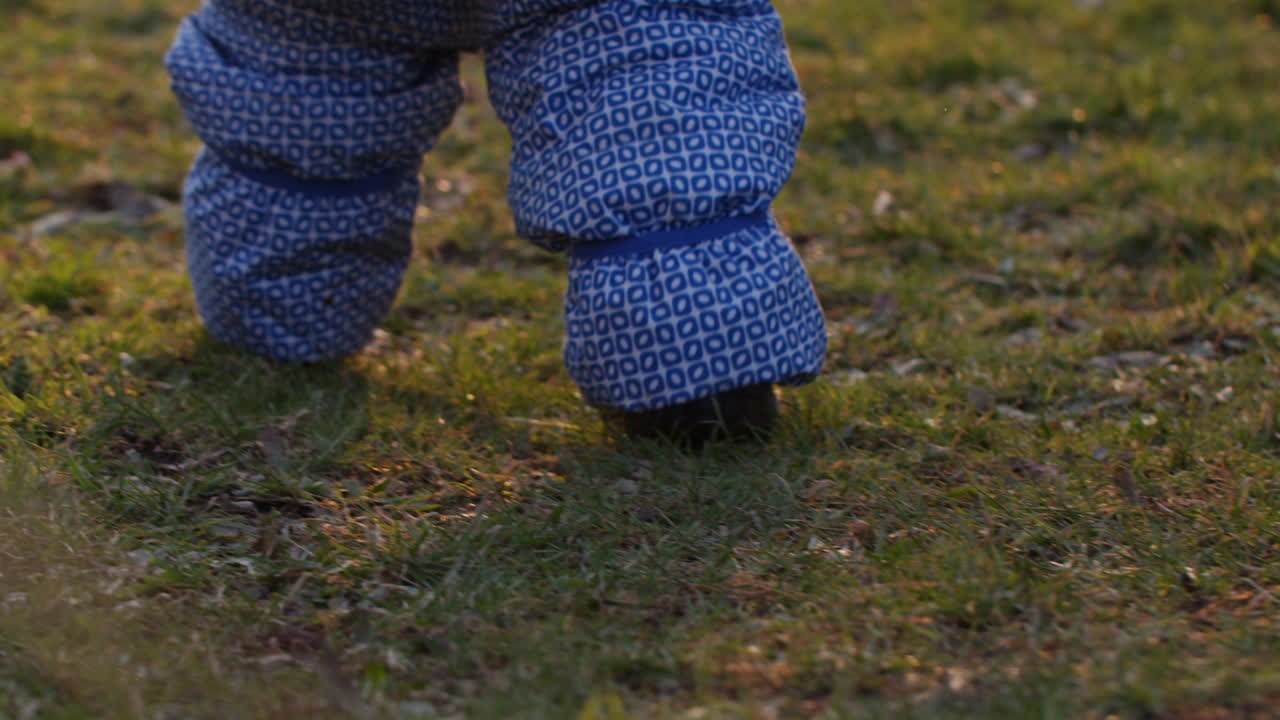 primer plano de un niño que lleva un traje de nieve caminando sobre la hierba en la hermosa luz del atardecer
