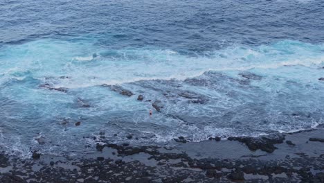young man swims through foamy ocean waters near lava rock coast, canary islands