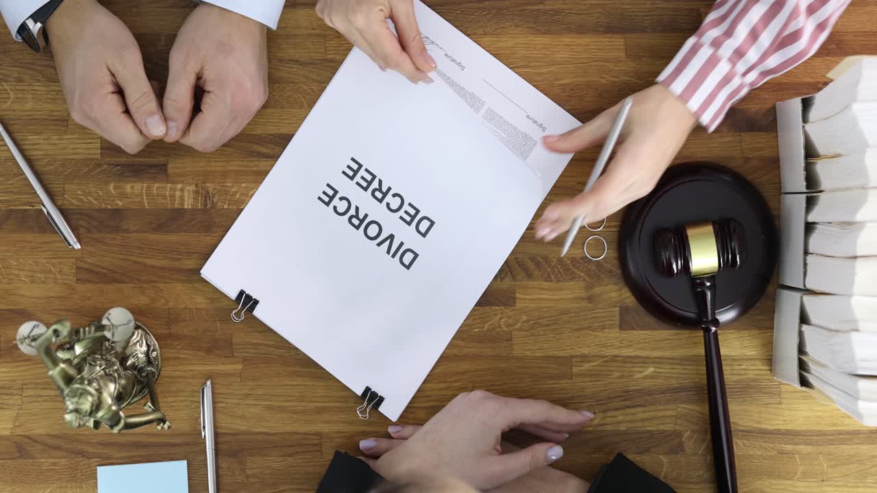 Hands signing a divorce decree with legal symbols and wedding rings