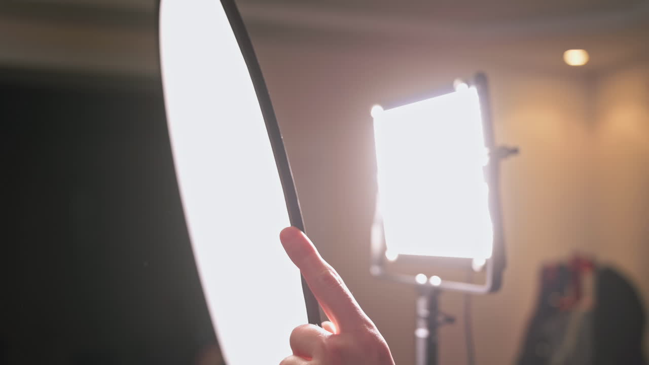 Serious young camera assistant holding diffuser near the light