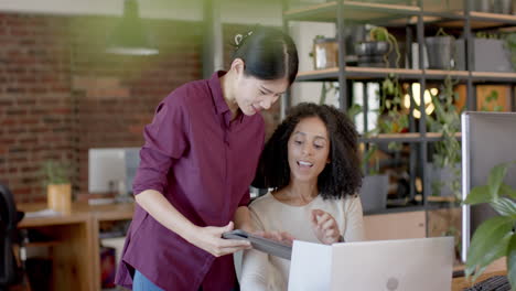 Happy-diverse-casual-businesswomen-using-tablet,-laptop-and-talking-in-office-in-slow-motion