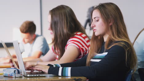 Vista-Lateral-De-Estudiantes-Universitarios-Sentados-En-Un-Escritorio-Usando-Computadoras-Portátiles-En-El-Aula