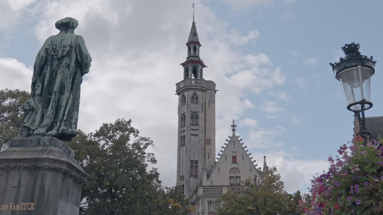 A scenic view of the historic architecture of Bruges' Jan van Eyckplein, featuring the slender Gothic tower of the Poortersloge (Burghers' Lodge)