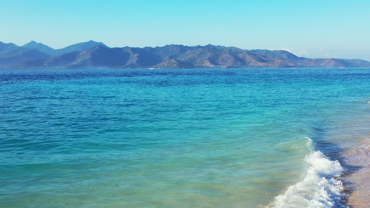 발리의 산지평선이 있는 모래 해변에서 흔들리는 푸른 청록색 바다의 맑고 활기찬 물이 있는 평화로운 바다