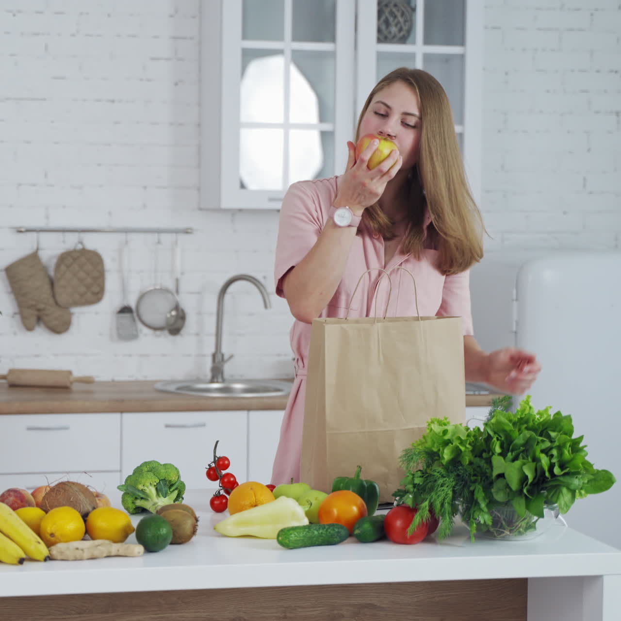 Happy housewife with fresh fruit and vegetables in the kitchen. Young woman unpack organic food from paper bag at home.