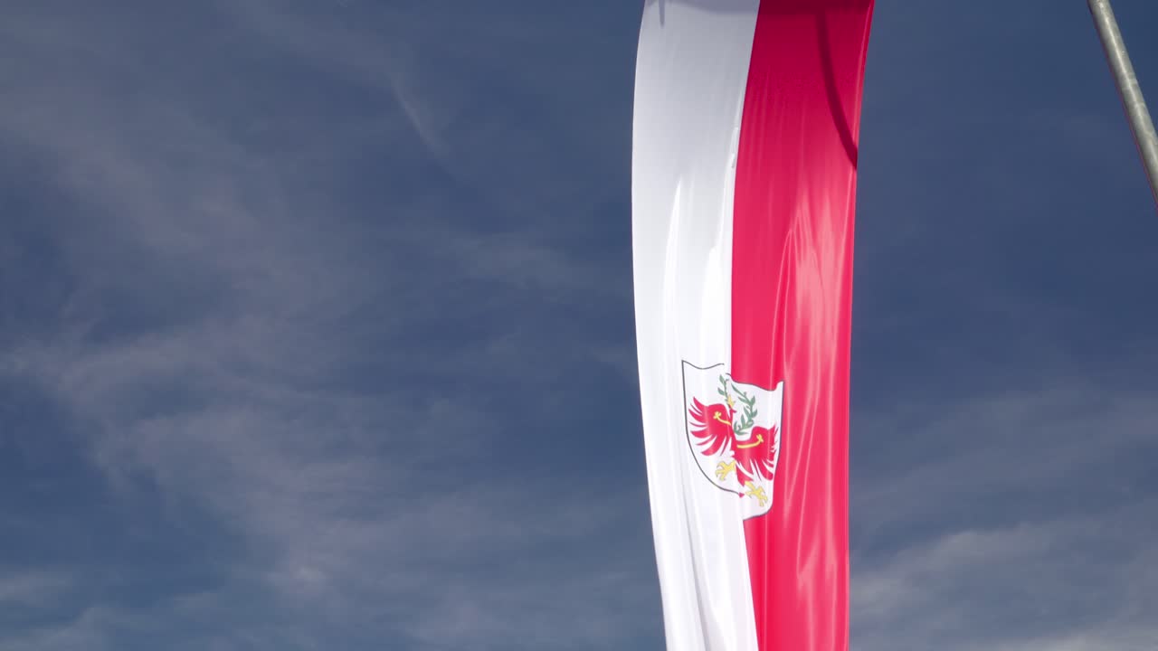 The South Tyrolean flag waves in the wind against a blue sky with streaks of clouds as a background