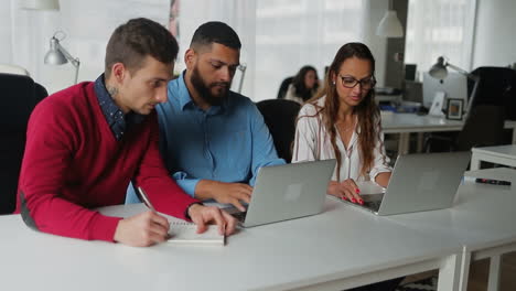 Manager-Nutzen-Laptops,-Während-Ihre-Kollegen-Notizen-Im-Block-Machen.