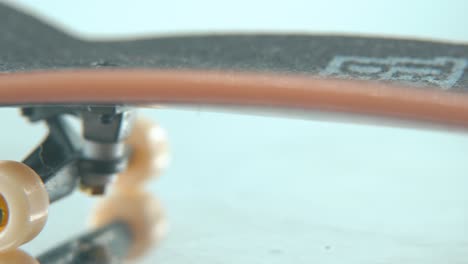 a macro detailed follow shot of a mini skateboard, tiny white wheels, fingerboard on a 360 rotating stand, shiny mirror reflection, professional lighting, cinematic 4k video pan right