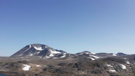 high altitude aerial view from drone over water looking toward shore and distant mountain with patches of snow