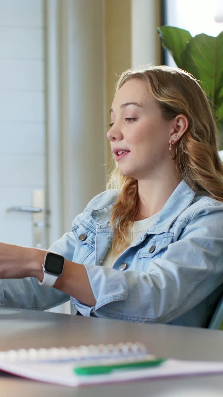 Vertical video: Answering offscreen prompt, woman in denim jacket gesturing at meeting, using pad