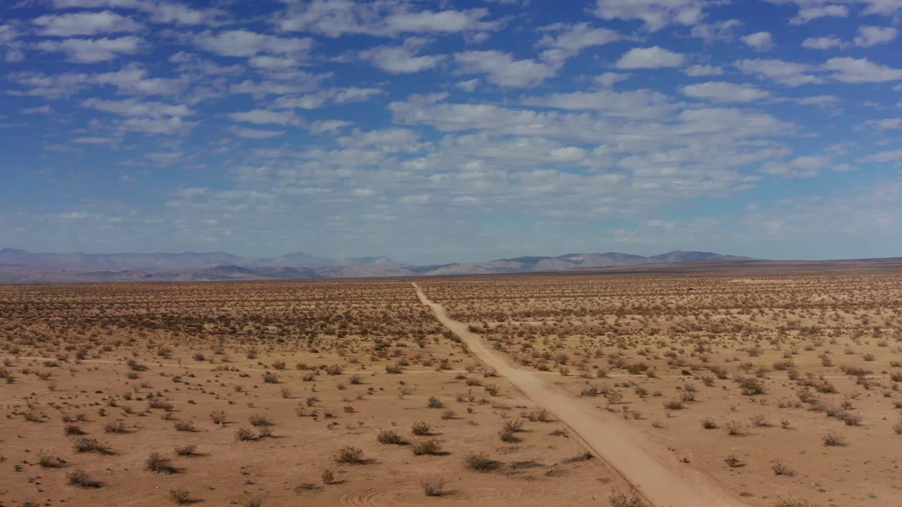 el levantamiento aéreo retrocede sobre el camino de tierra en el interminable desierto de mojave