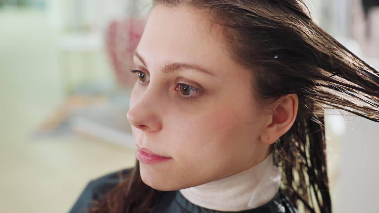 primer plano del perfil de un cliente al que le aplican acondicionador y lo peinan; el estilista alisa el cabello húmedo desde la raíz hasta las puntas, en un tranquilo salón con luz natural que entra por la ventana y donde se emplean técnicas muy precisas