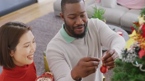 video of happy diverse couple decorating christmas tree at home