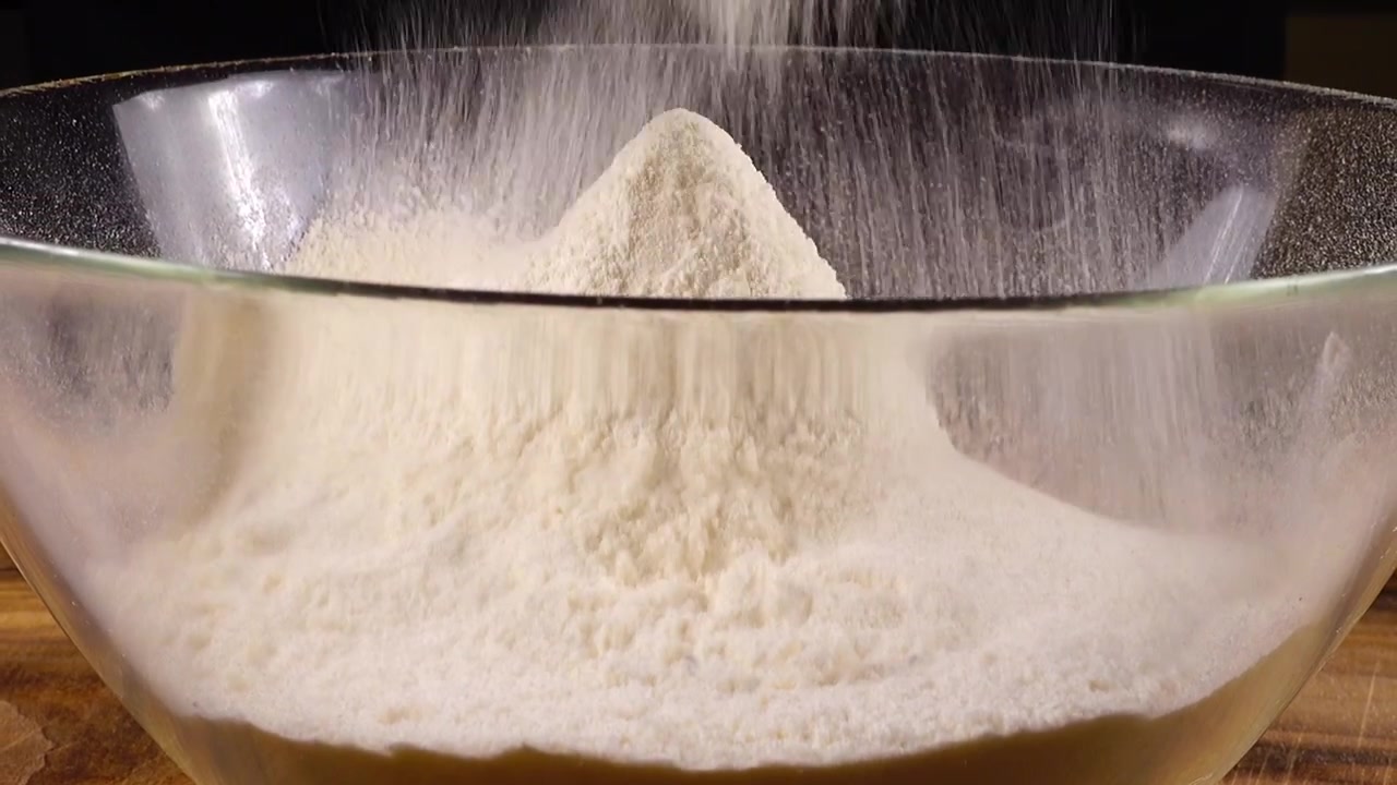 Mengayak tepung menggunakan saringan ke dalam mangkuk kaca di dapur.