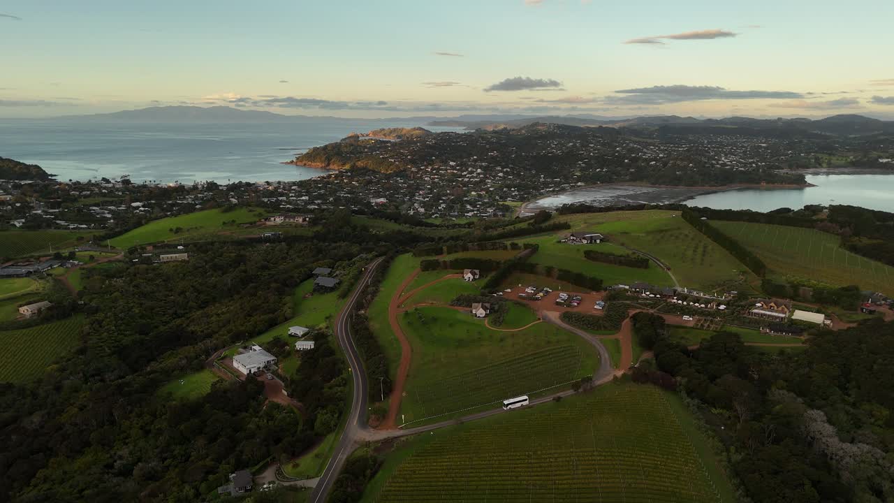 Coastal town, vineyards and bay at sunset, Waiheke Island, New Zealand. Aerial backward