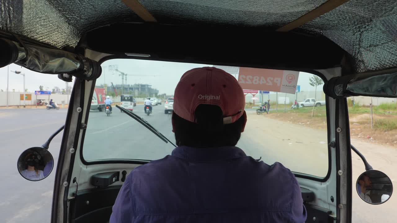 Traveling through a lively rural environment while seated in an auto rickshaw, capturing the journey along a busy road filled with vehicles and activity in cambodia