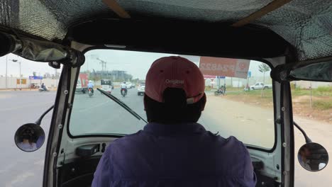 traveling through a lively rural environment while seated in an auto rickshaw, capturing the journey along a busy road filled with vehicles and activity in cambodia
