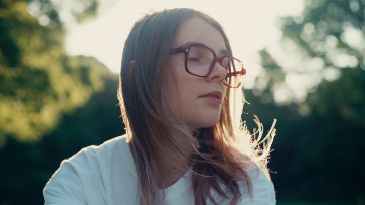 Park portrait under clear sky. Girl with wind-tossed hair and warm sunlight.
