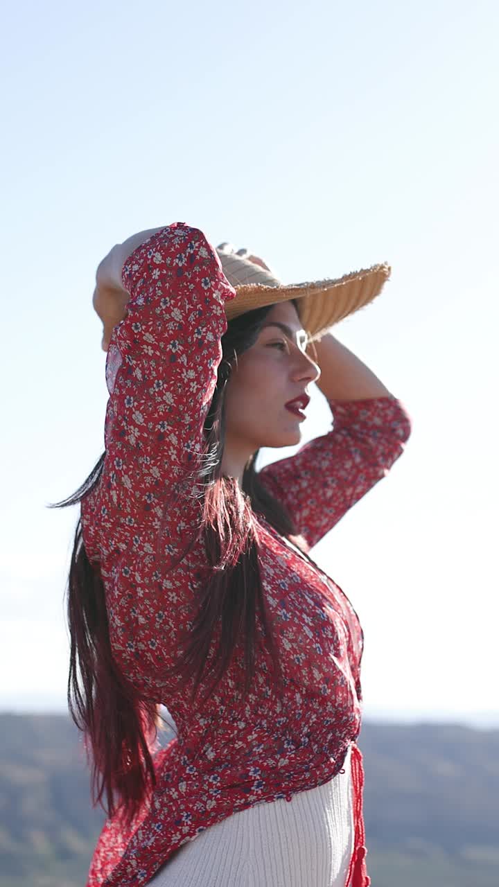 A woman in a red floral dress and straw hat enjoying the sun outdoors