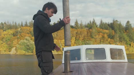 young man installs chimney pipe for wood burning stove exterior roof of wooden boat