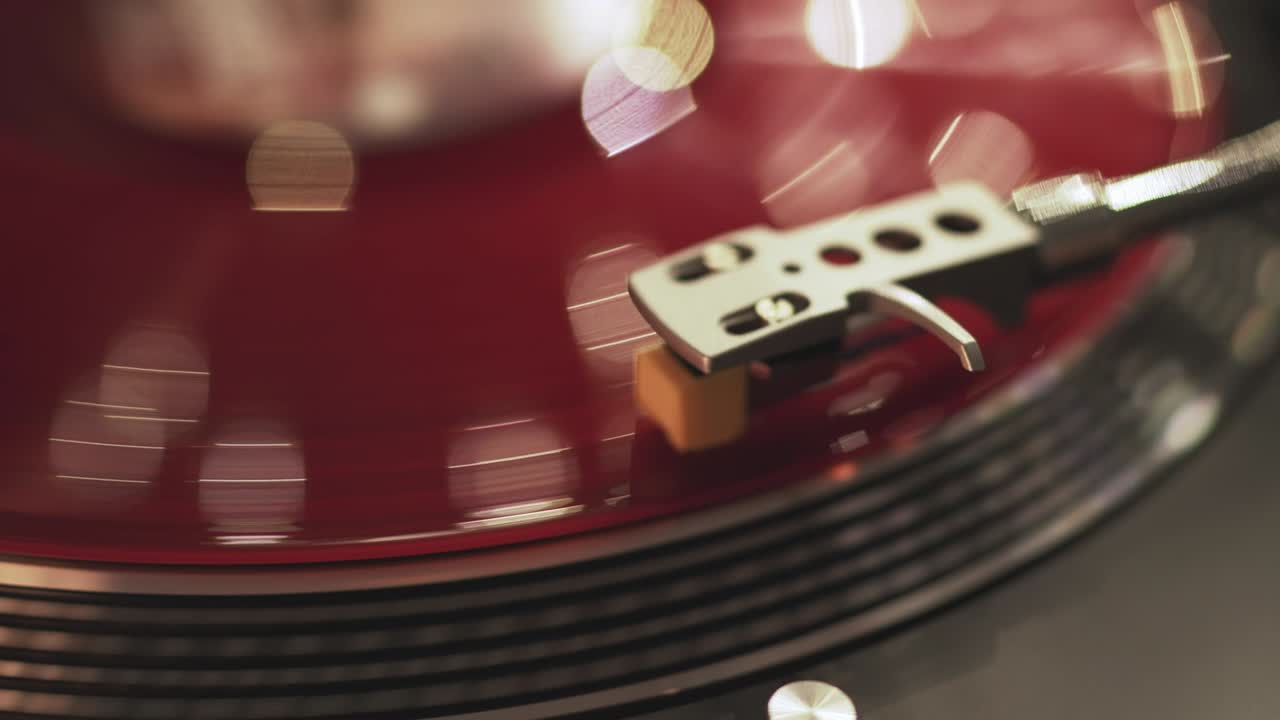 저녁 시내의 불빛이 보케가 있는 해가 지는 배경의 비닐 플레이어: 소녀의 손은 바늘을 회전하는 빨간 비닐 판에 놓는다.