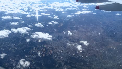 Cityscape-through-airplane-window,-clouds-casting-shadows-on-landscape,-sunny-day,-aerial-view