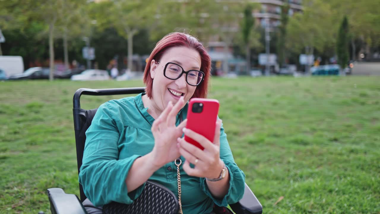 Donna in carrozzina elettrica che ride mentre usa lo smartphone al parco