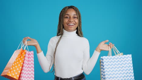 happy young woman showing off shopping bags on blue background
