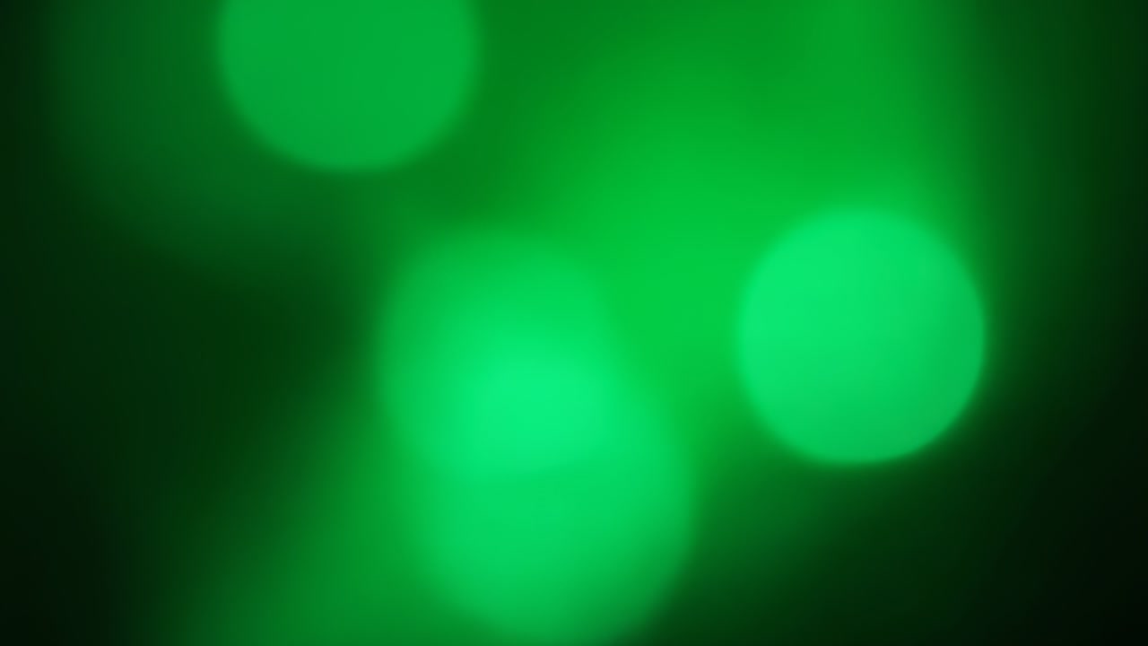 Un grappolo di bokeh verde che fluttua attraverso uno studio buio mentre l'obiettivo sfoca, creando un bagliore a LED.