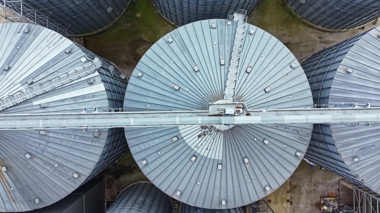 Silosy zbożowe widziane z góry, duże metalowe konstrukcje na terenie rolniczym w ciągu dnia.