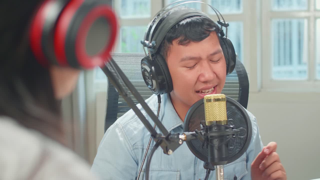 Over Shoulder View, Young Asian Boy In Headphones Singing Into Microphone While Recording Podcast With Kid Girl Host In Studio