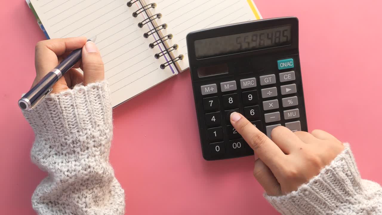 mujer usando una calculadora y escribiendo en un cuaderno