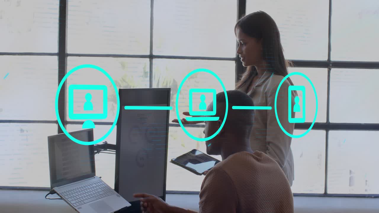 Standing woman showing tablet, expanding cyan icons while seated man tapping laptop, syncing tech