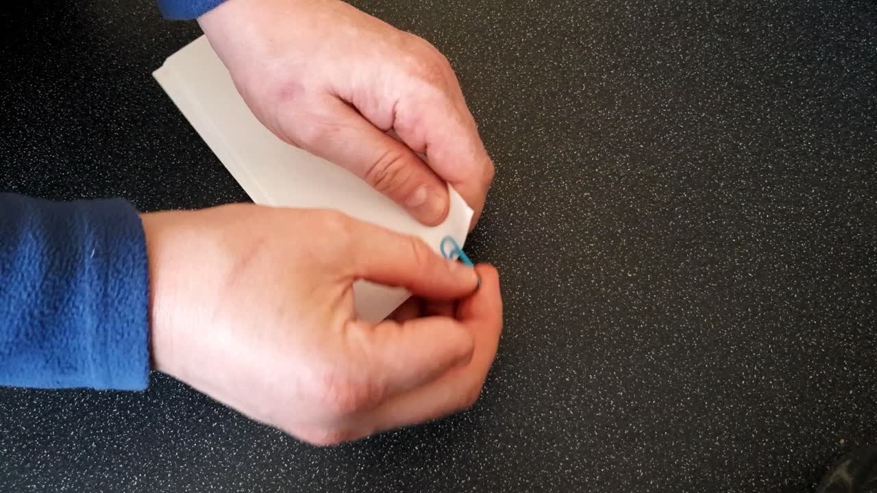 Male with a partially amputated index finger on his right hand putting a blue paper clip on som strips of white paper