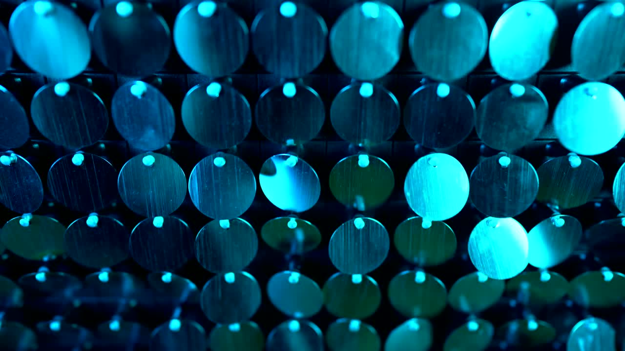 Shiny kinetic surface panel illuminated by blue light in luxury boutique. Flickering background for interruptions or text savers. Mirror sequins sway by wind blowing.