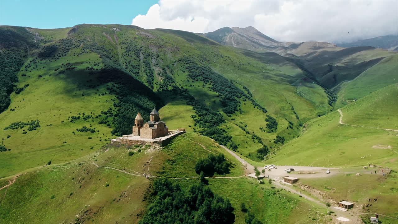 Aerial drone view of Gergeti Trinity Church in Georgia. Caucasus Mountains, church located on the top of a hill, greenery, valley