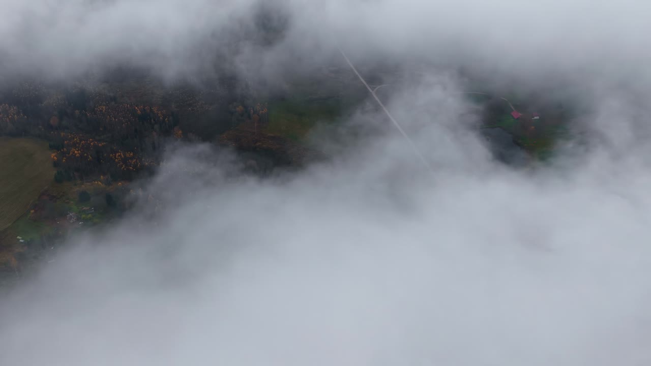 Drone-luchtlandschap met mistige, bewolkte mist in de lucht die een landelijk Lets stadje in de buitenwijken onthult met hoofdweg nabij bosbomen en landbouwgrond, een plattelandsmeer in Europa, reizen, weer, natuur buitenshuis