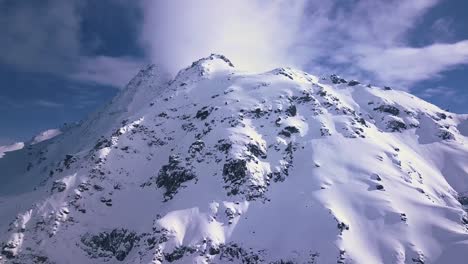 Aerial-drone-shot-of-a-white-snowy-peak-among-the-alps-and-mountains-above-the-vacation-resort-town-of-Verbier,-Switzerland