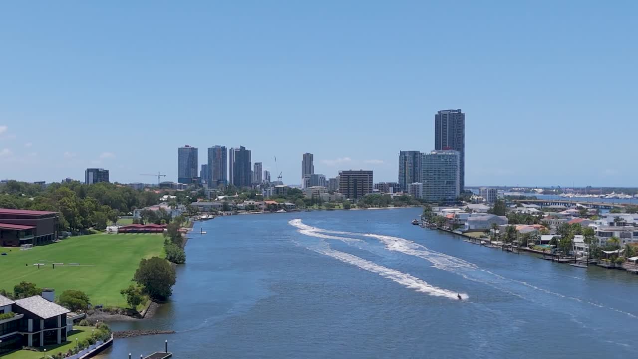 A tranquil river scene with lush greenery and distant skyscrapers under a clear blue sky.