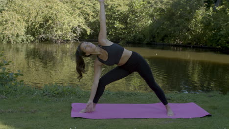 young woman doing sun pose yoga exercises near pond