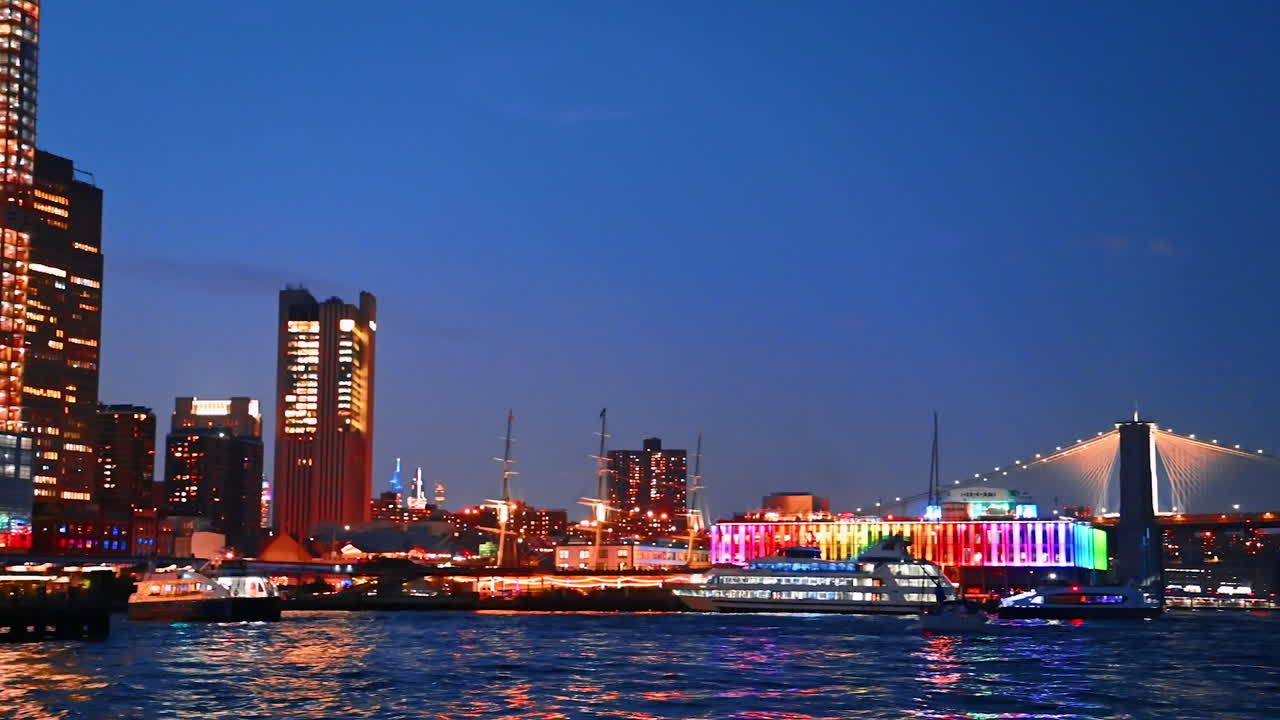 Fantastic illumination of the buildings and streets at the waterfront of the East River. Diverse boats arrive to the pier at dusk time