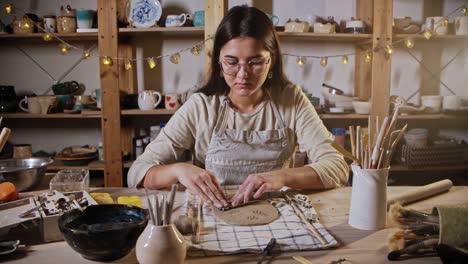 young woman potter makes a design on the clay plate using a stamp