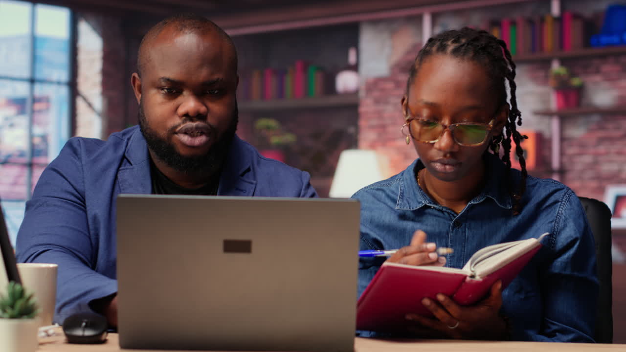 Black remote employees organizing calendar appointments using laptop and ledger