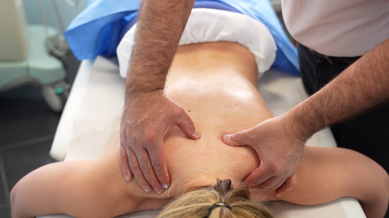 las manos del fisioterapeuta masajeando la espalda de una paciente acostada en la cama en la clínica